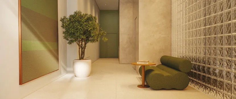 Lobby do Alameda Mará Smart, em Moema, com parede de tijolos de vidro, poltrona verde, mesa lateral e vaso com árvore.