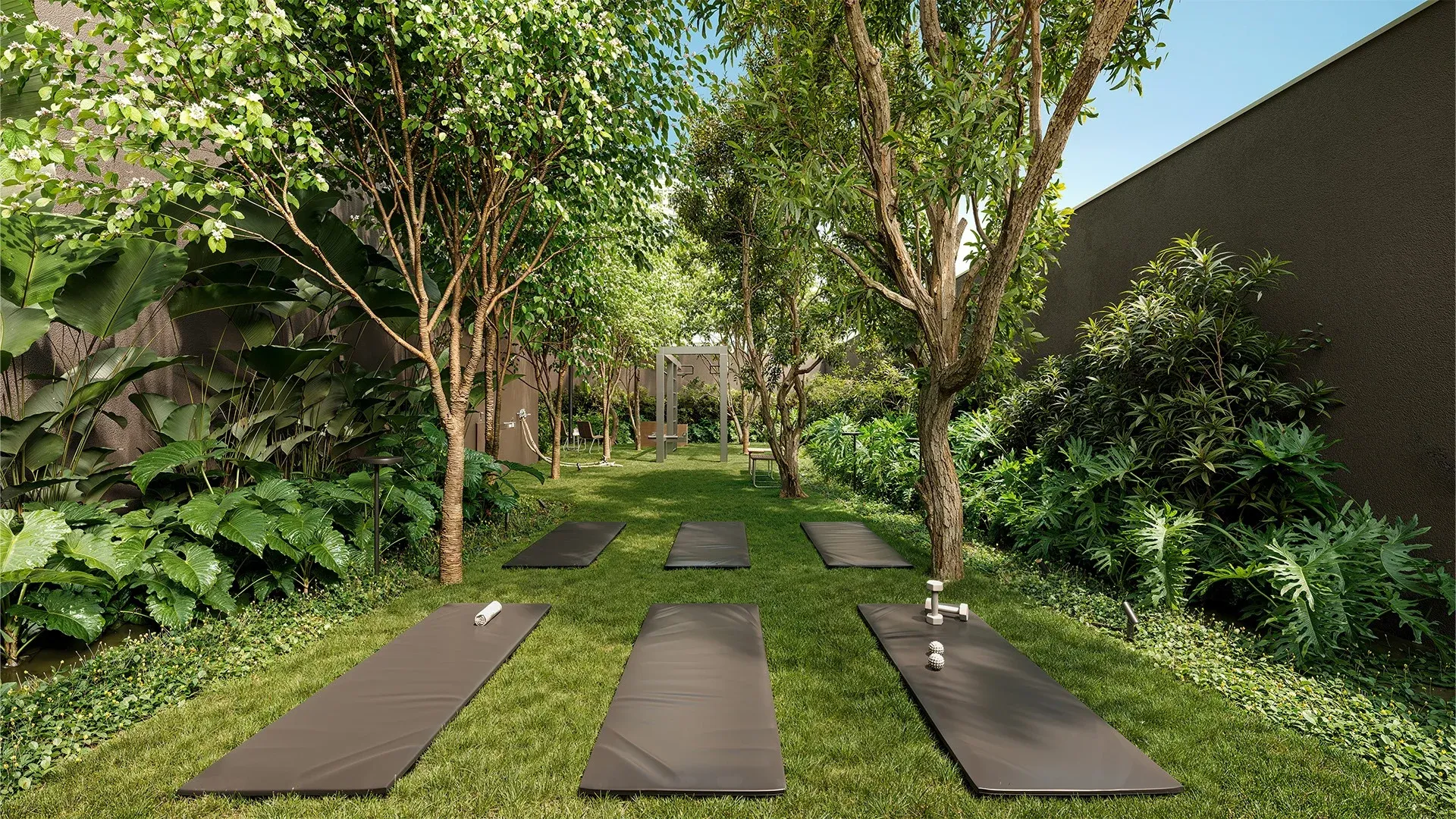 Área de fitness e yoga outdoor no térreo do Alameda Mará, Gamaro, em Moema, com tapetes de yoga e pesos sobre o gramado sombreado.